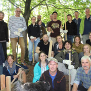 Betriebsausflug einmal anders: Mit Rangern im Einsatz für die Natur Eine Gruppe Erwachsener mit Arbeitshandschuhen, Holzpfählen und großen Hammern sitzt und steht an einem Hang im Wald.