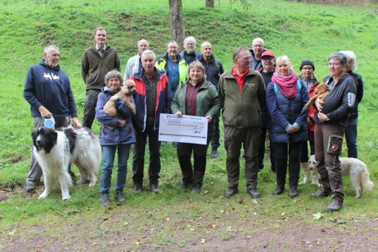 Eine Gruppe mit etwa 15 Erwachsenen und Hund, in erster Reihe eine Frau mit großem Scheck Eine Gruppe mit etwa 15 Erwachsenen und Hund, in erster Reihe eine Frau mit großem Scheck