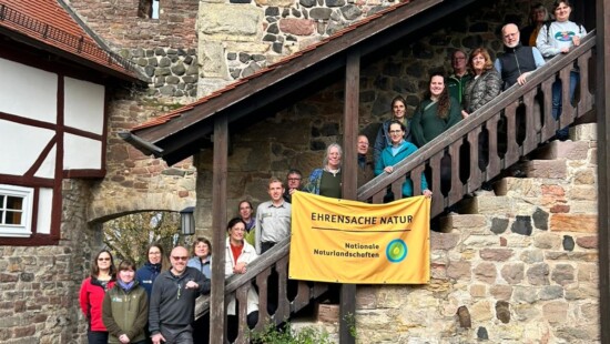 und 20 Erwachsene stehen auf einer Treppe, eingefasst in eine alte Mauer, vor sich ein Banner "Ehrensache Natur".